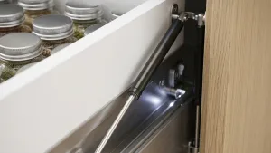 A close-up of a black electric actuator installed inside a kitchen cabinet drawer to provide smooth, automated movement.