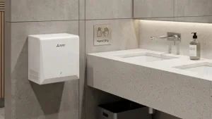 A compact, wall-mounted energy saving hand dryer located next to a minimalist stone vanity and sink in a high-end commercial bathroom.