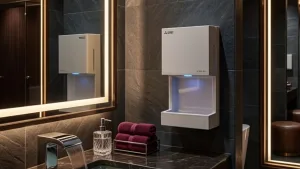 A white wall-mounted hand dryer with a blue indicator light, providing a sustainable alternative to paper towels in a luxury dark-tiled bathroom.